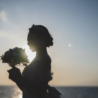 夕日を背にブーケを持って立つ、ティアラを付けた花嫁の横顔のシルエット。海辺で撮る洋装前撮りの一枚
