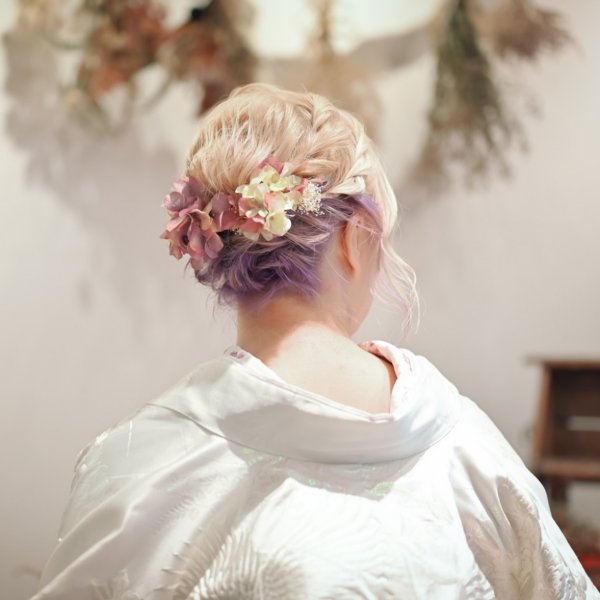 ブロンドに紫のインナーカラーを施した髪に、くすみピンクの紫陽花をあしらった編み込みまとめ髪。白無垢姿の花嫁の後ろ姿クローズアップ。