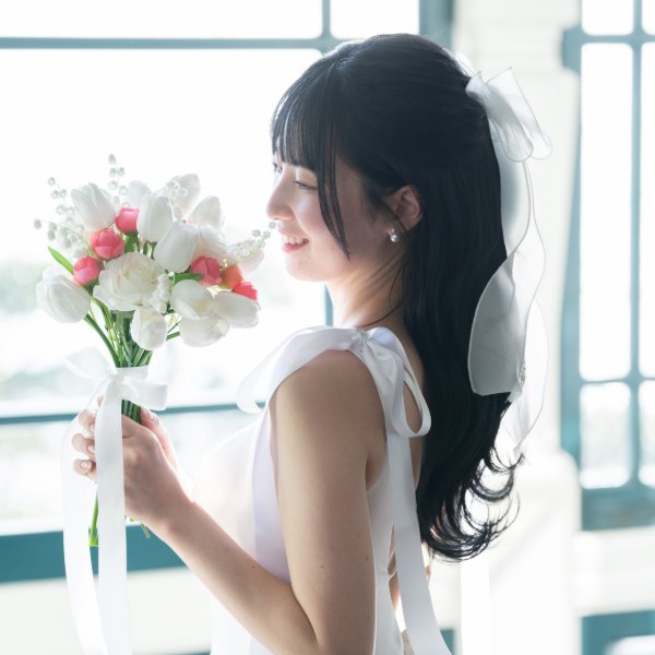 大きな白いリボンを髪に飾り、白とピンクのチューリップのブーケを手にした花嫁の横顔クローズアップ。