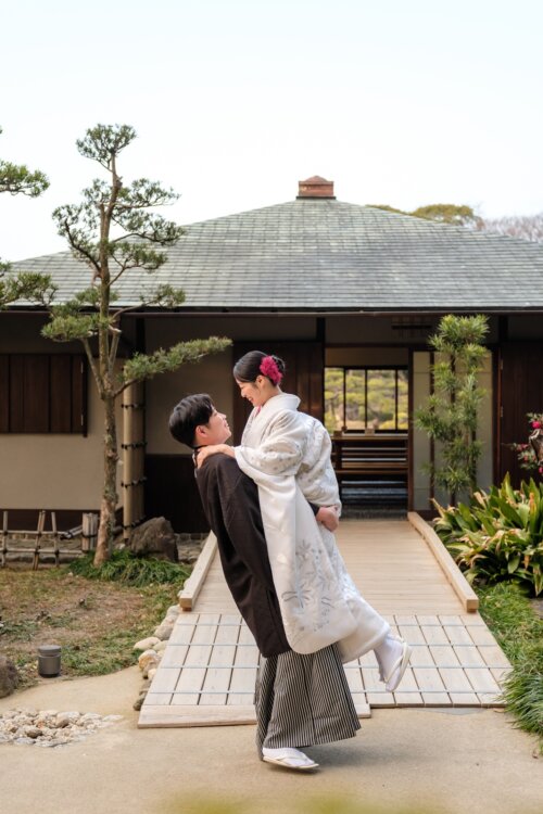 日本家屋へ続く石畳で、白無垢の花嫁をお姫様抱っこする紋付袴の新郎。日本庭園でのフォトウェディング
