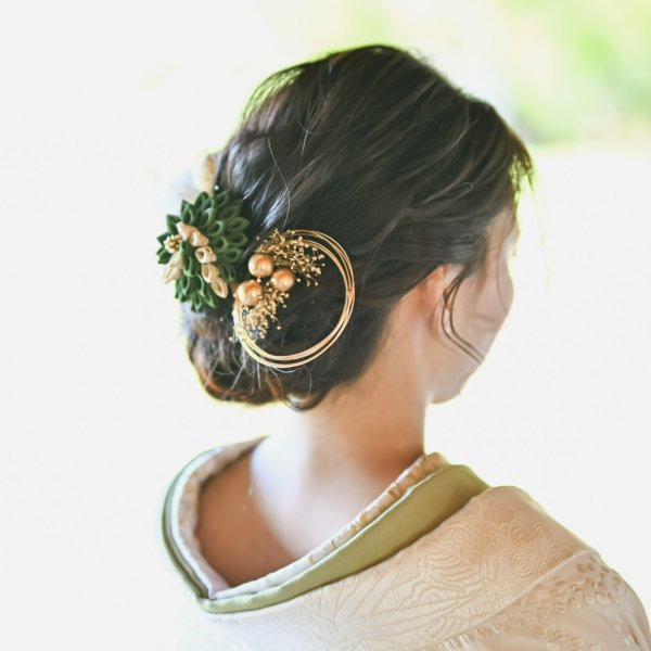 和装向けアップスタイルのヘアメイク。緑の花モチーフと金の輪飾り、パールをあしらった和風の髪飾りのクローズアップ。