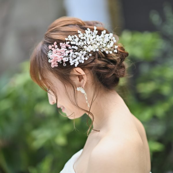 ドレス向けアップスタイルのヘアメイク。白とピンクの小花をあしらったヘッドアクセサリーと、ドロップ型のイヤリングのクローズアップ。