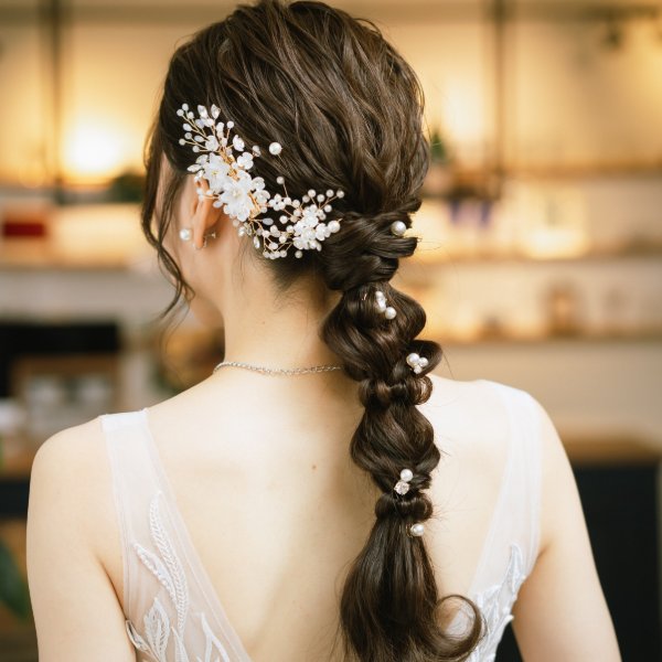 白い小花とパールをあしらった編み下ろしポニーテール。レースのドレス姿の花嫁の後ろ姿クローズアップ。
